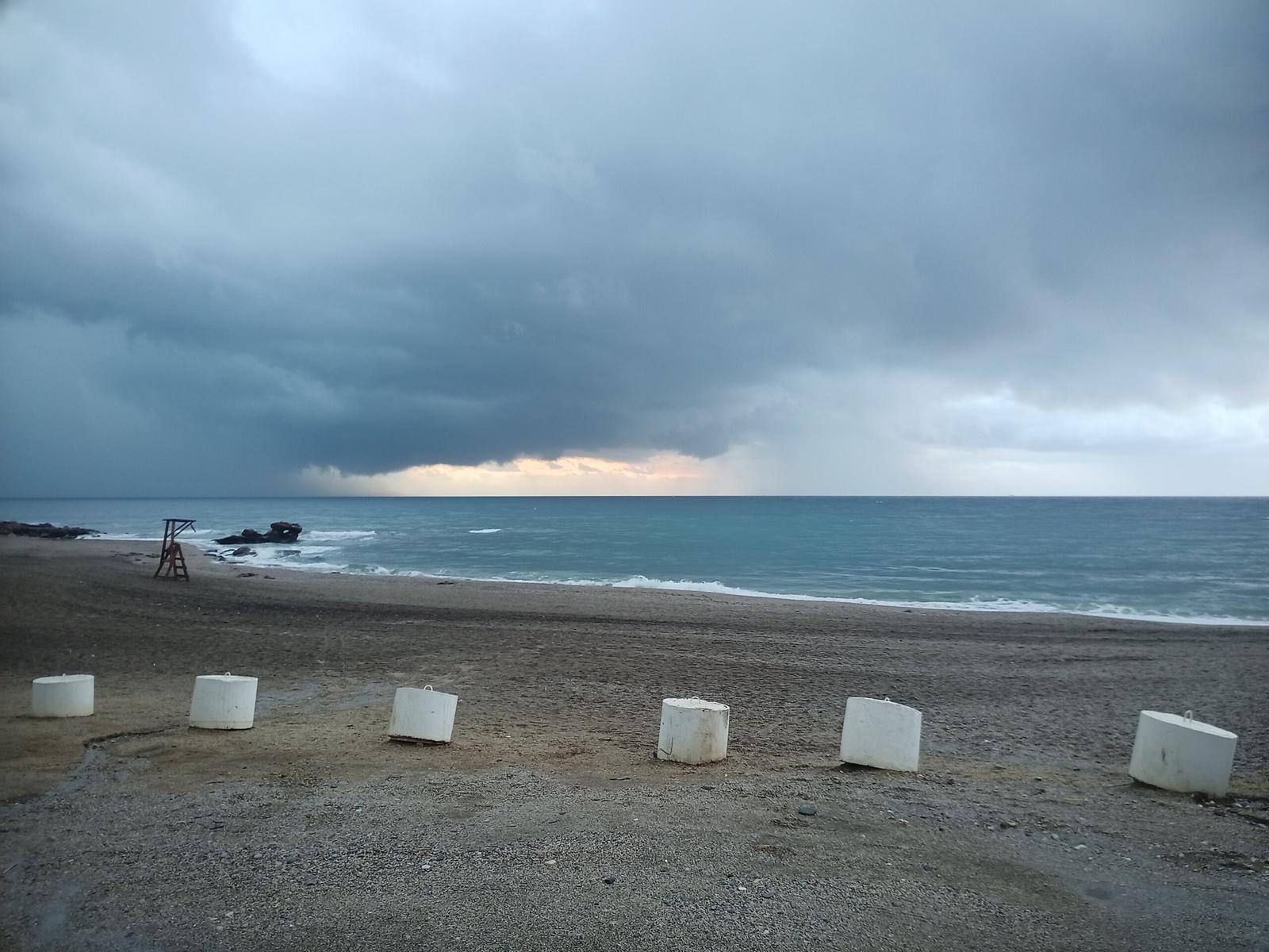 Storm clouds gather over a view of a beach with sea and large white stones on the beach